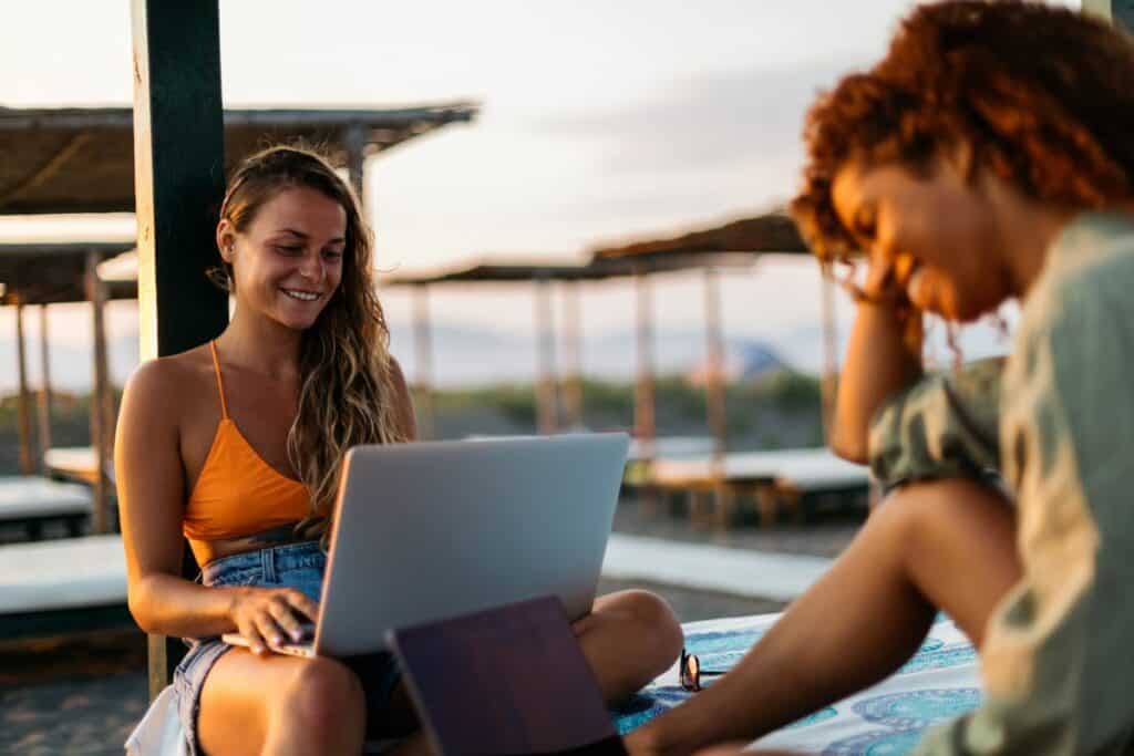 Två unga kvinnor utomhus i varmt klimat, med laptops